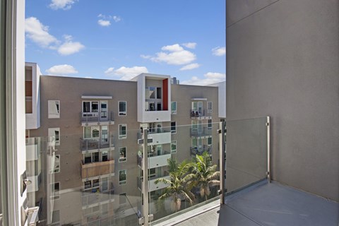 A balcony with a glass railing and a view of a building with multiple windows.