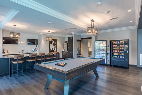 A pool table is in the middle of a room with a bar and a refrigerator.
