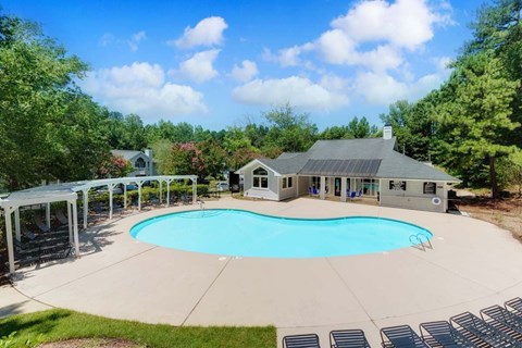 A large outdoor swimming pool surrounded by a white pergola and a house in the background.