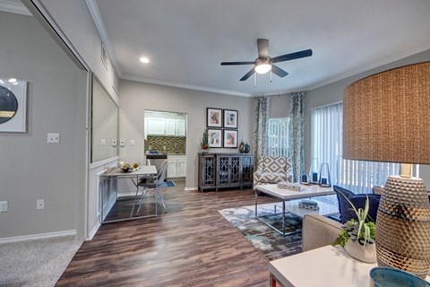 A well-lit living room with a wooden floor and a ceiling fan.
