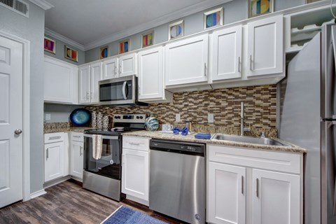 A kitchen with white cabinets and a stone backsplash.