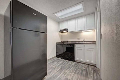 A black refrigerator is in a kitchen with white cabinets and a black oven.