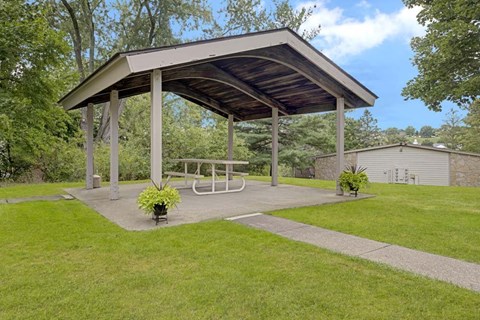 A pavilion with a picnic table is surrounded by a grassy area.