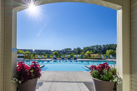 A view of a pool through an archway with red flowers in the foreground.