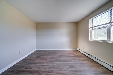 Empty room with wooden flooring and a window on the right side.