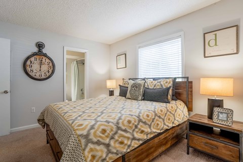 A bedroom with a patterned bedspread, a clock, and a nightstand with a lamp.