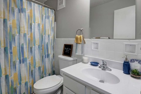 A bathroom with a white toilet, a white sink, and a shower curtain with a yellow towel hanging on the towel rack.