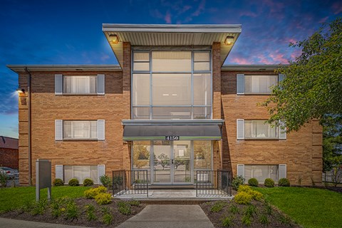 The image shows a modern two-story building with a large glass entrance and a brick facade.