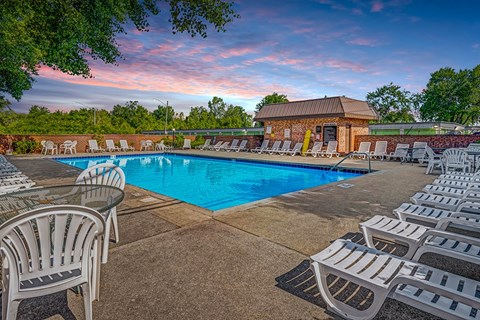 A pool surrounded by chairs and a building in the background.