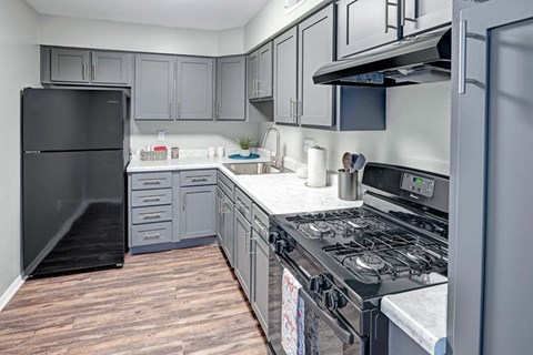 A black refrigerator stands in a kitchen with wooden flooring.