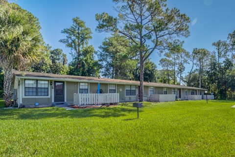 A row of houses with green lawns and trees in the background.