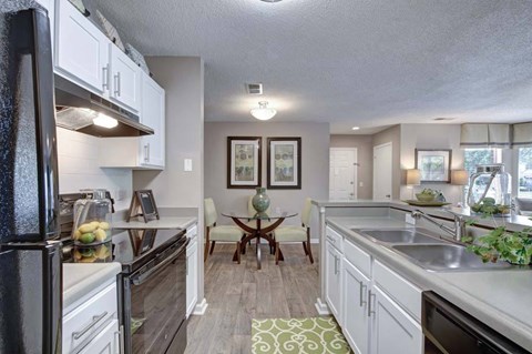 A kitchen with a black refrigerator and stove, a dining table with chairs, and a sink with a faucet.