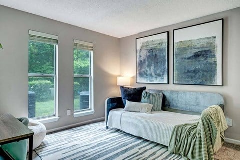 A bedroom with a bed, a couch, and two paintings on the wall.