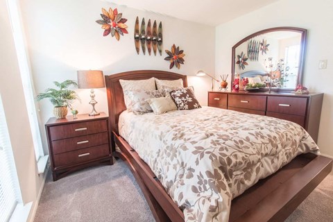 A bedroom with a large bed, a mirror, and a dresser with a plant on it.