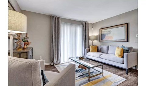 A living room with a grey couch, a glass coffee table, and a painting on the wall.