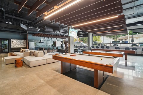 A pool table is in the middle of a room with a couch and a bar.