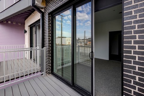 A balcony with a glass door leading to a room.