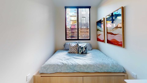 A bedroom with a bed, pillows, and two framed pictures on the wall.