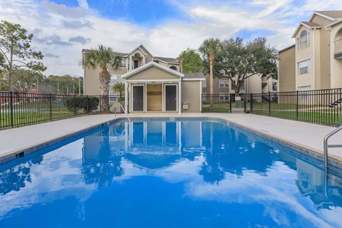 A swimming pool in front of a house with a black fence.