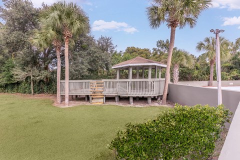A gazebo sits in the middle of a grassy area with palm trees.