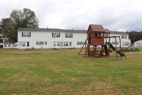 A playground with a wooden swing set in front of a white building.