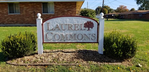 A sign that says "Laurel Commons" stands in front of a brick building.