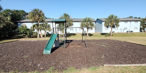 A playground with a green slide in the foreground and a building in the background.