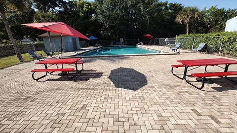 A pool surrounded by red umbrellas and benches.
