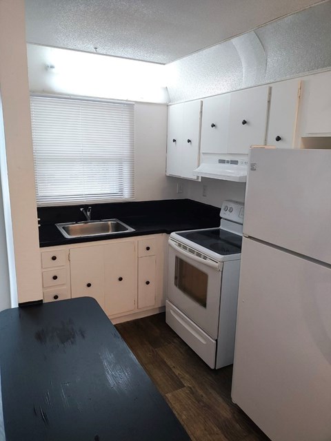 A kitchen with white appliances and black countertops.