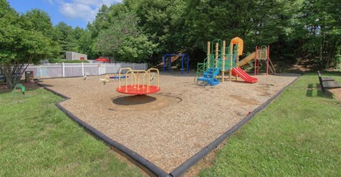 A playground with a red and blue slide, a yellow and green slide, and a yellow and blue climbing frame.