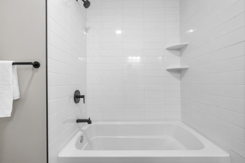 A white bathroom with a white tub and a white towel hanging on the door.