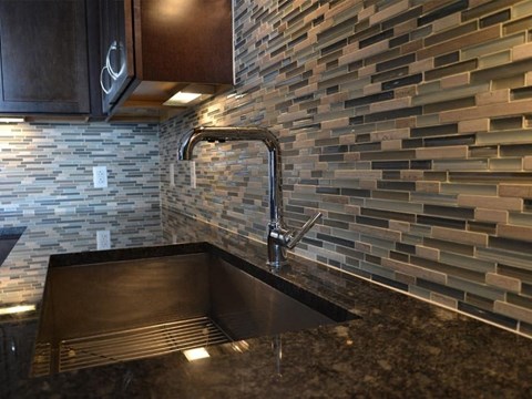 A kitchen with a sink and a wall of tiles.