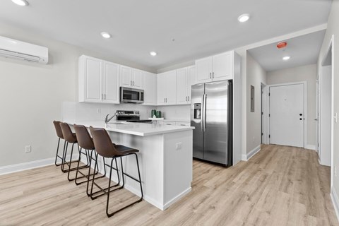 A kitchen with white cabinets and a white island with brown barstools.