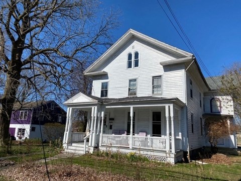 A white house with a porch and a tree in front.