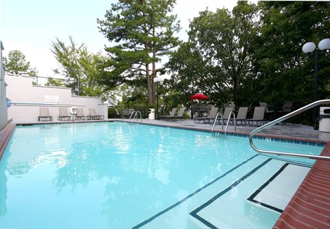 A swimming pool with a red umbrella and trees in the background.