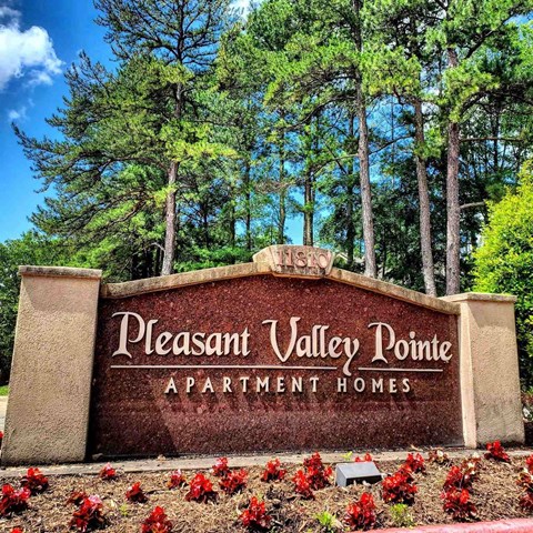 A sign for Pleasant Valley Pointe Apartment Homes is surrounded by flowers and trees.