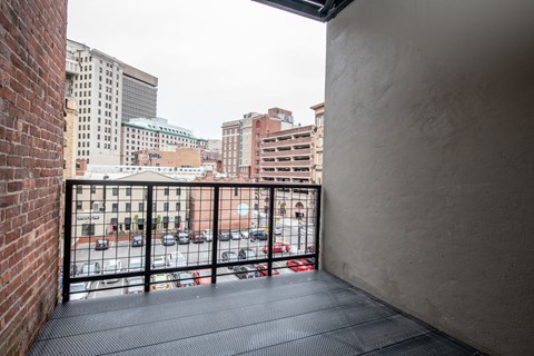 A balcony with a black railing overlooks a parking lot and buildings.
