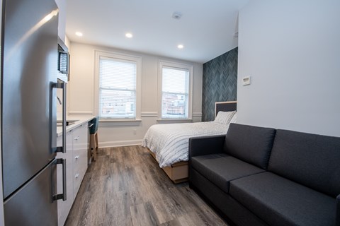 A modern kitchen with a refrigerator on the left and a grey couch in the middle of the room.