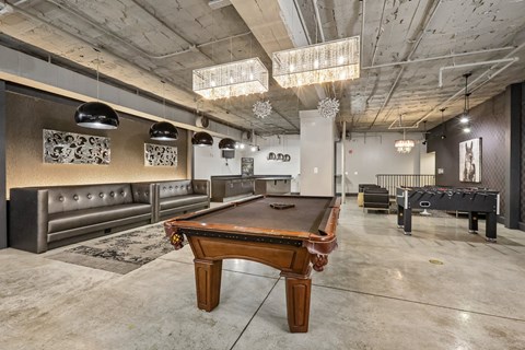 A pool table is in the middle of a room with a concrete floor and a concrete ceiling with lights.