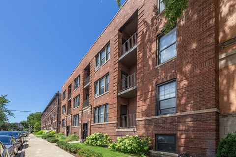 A red brick apartment building with green bushes in front.