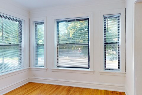 Three windows with blinds in a room with wooden floors and white walls.