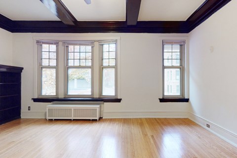 A room with wooden floors and white walls has a window with a view of trees.