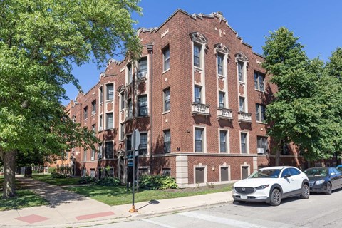 A white car is parked on the street in front of a red brick building.
