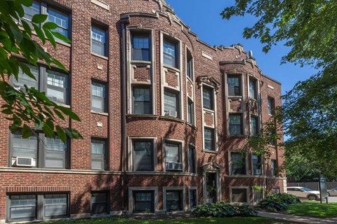 A large red brick building with many windows and a tree in front.