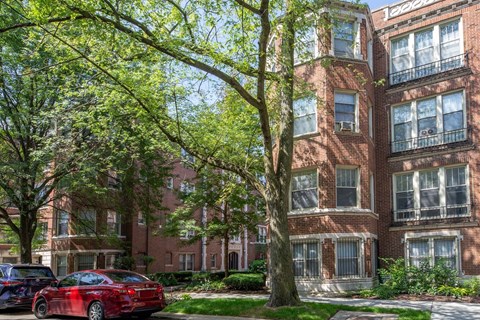 A red car is parked on the street in front of a brick building.
