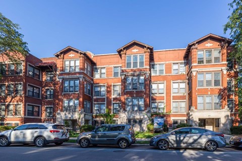 A large red brick building with multiple windows and cars parked in front.