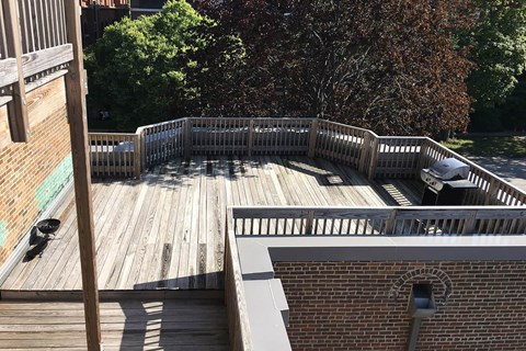A wooden deck with a white railing and a brick building in the background.