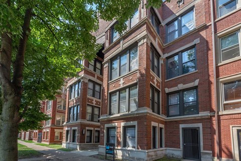 A tall red brick building with many windows and a tree in front.