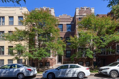 Three cars parked on a street in front of a brick building.