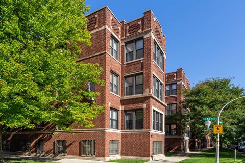 A tall red brick building with many windows and a tree in front.